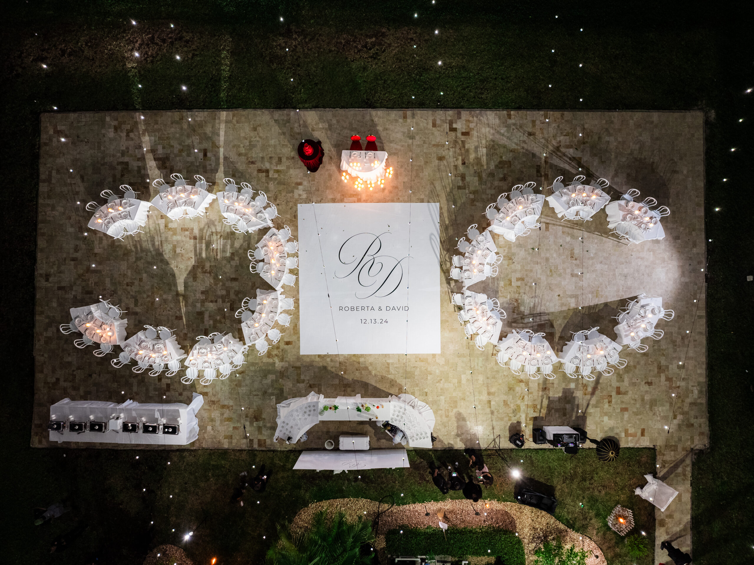 Outdoor wedding reception setup with circular seating, monogrammed dance floor, and ambient lighting at a private estate