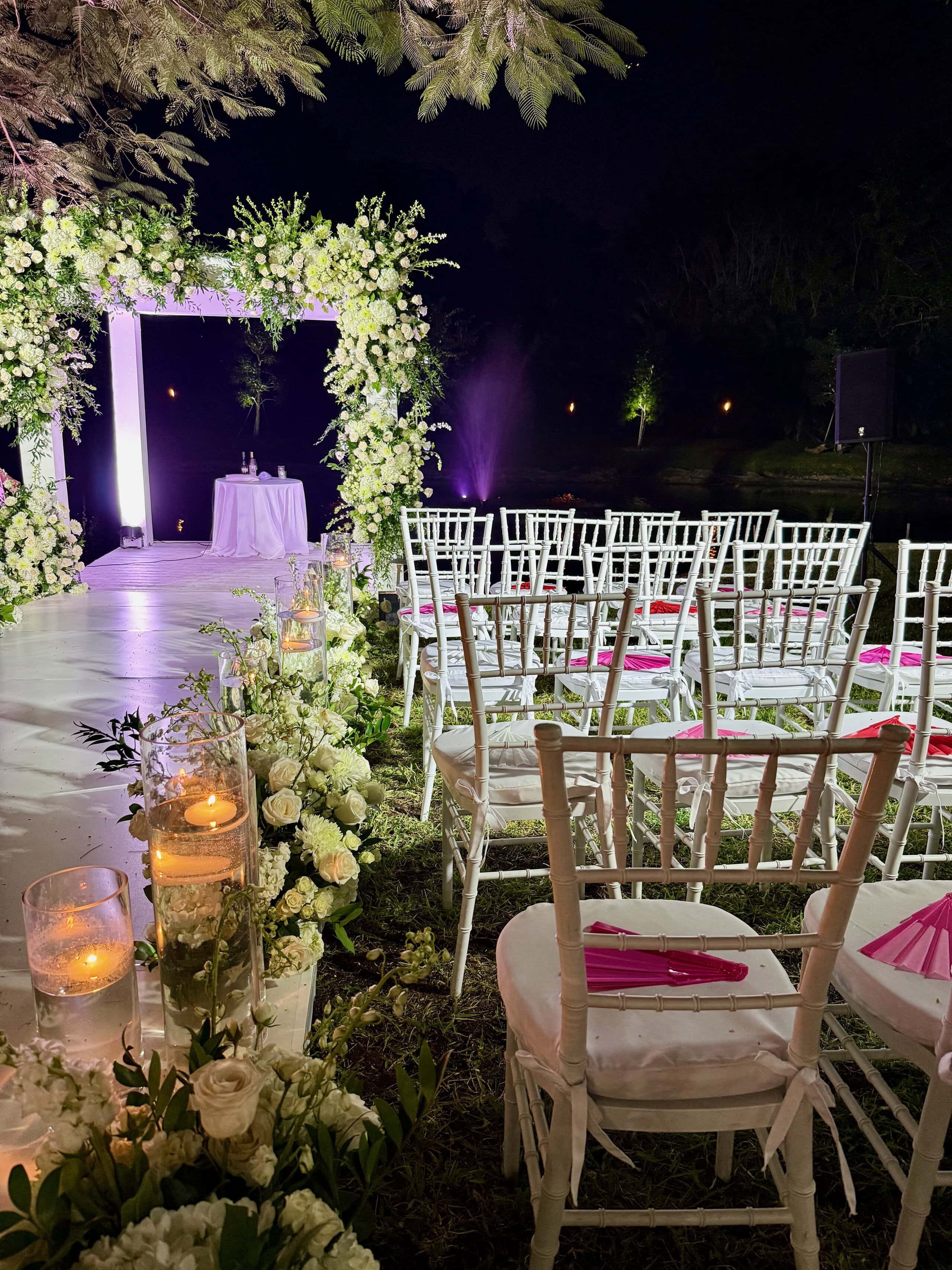 Candlelit wedding ceremony aisle with white floral arch at Saint Patrick Palace, a private estate wedding venue in South Florida.
