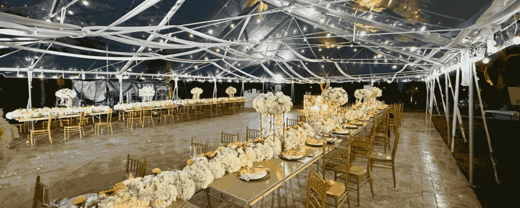 Nighttime view of a luxury wedding reception with long feasting tables, white hydrangea runners, and bistro lighting.
