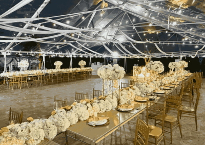 Nighttime view of a luxury wedding reception with long feasting tables, white hydrangea runners, and bistro lighting.