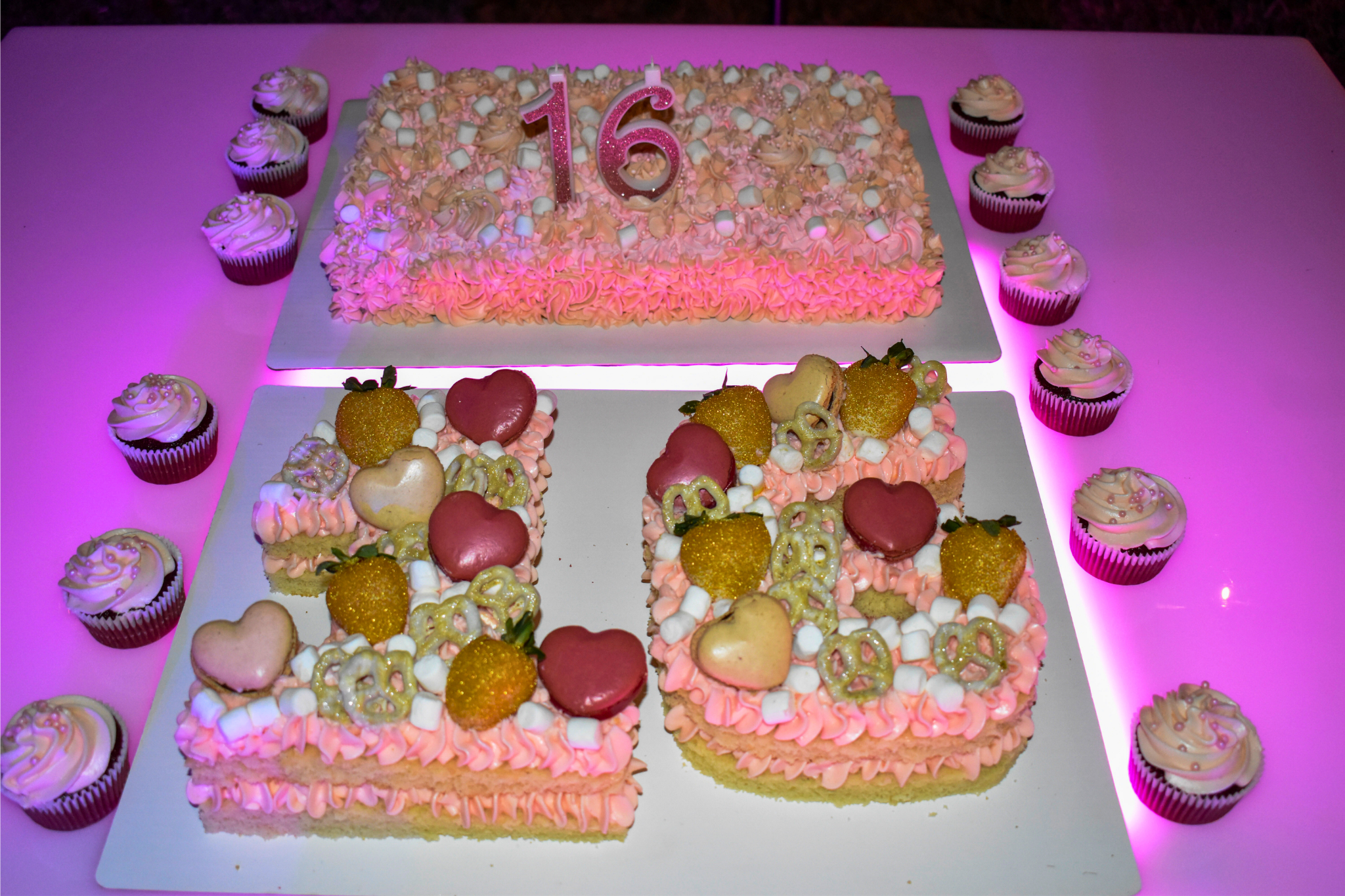 Sweet 16 cake and cupcakes decorated with pink frosting, glitter strawberries, and heart-shaped macarons.