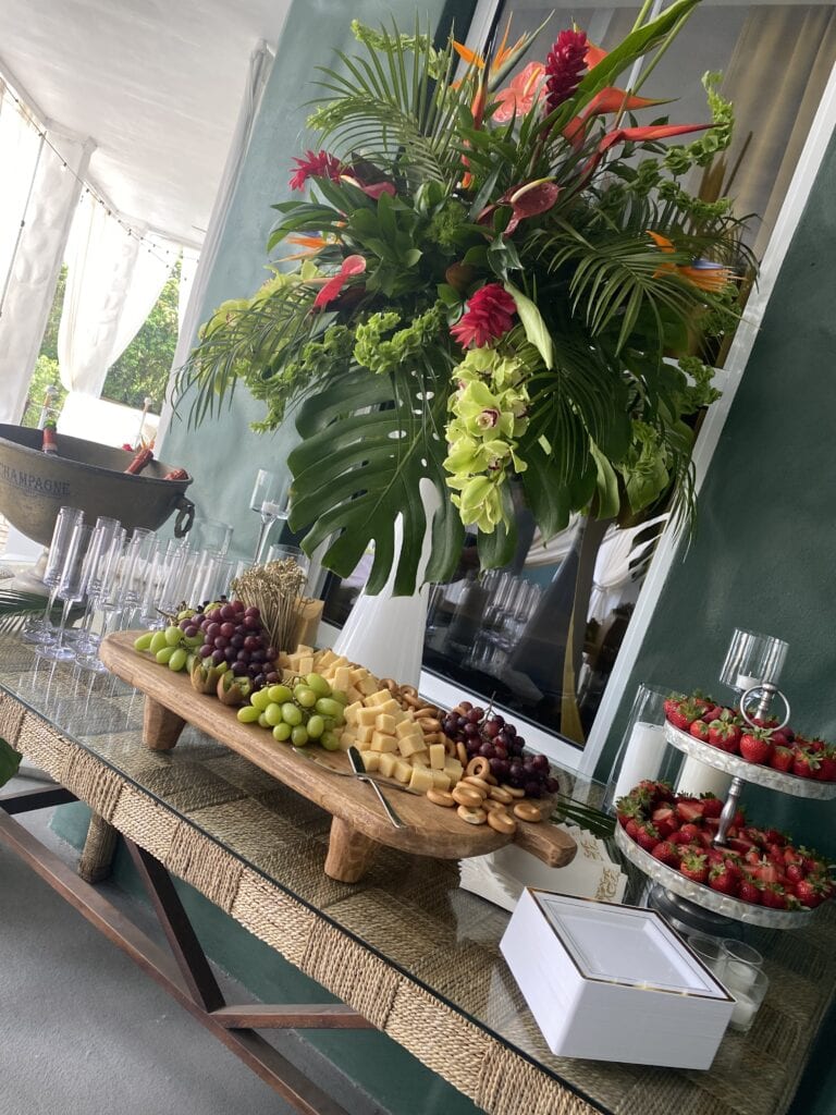 Tropical welcome display with champagne, charcuterie, and florals for a luxury 60th birthday garden brunch in South Florida.