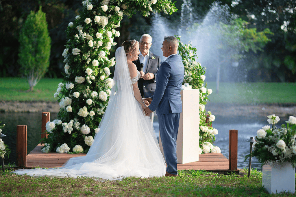 Bride and groom exchanging vows under floral arch by waterfront at Saint Patrick Palace outdoor wedding ceremony
