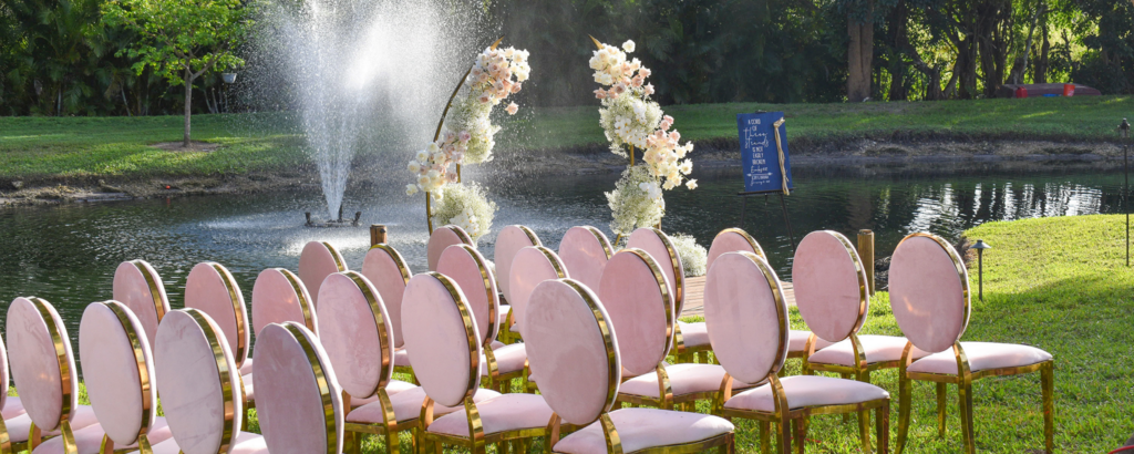 Outdoor waterfront wedding ceremony setup with pink velvet chairs and floral arches at Saint Patrick Palace