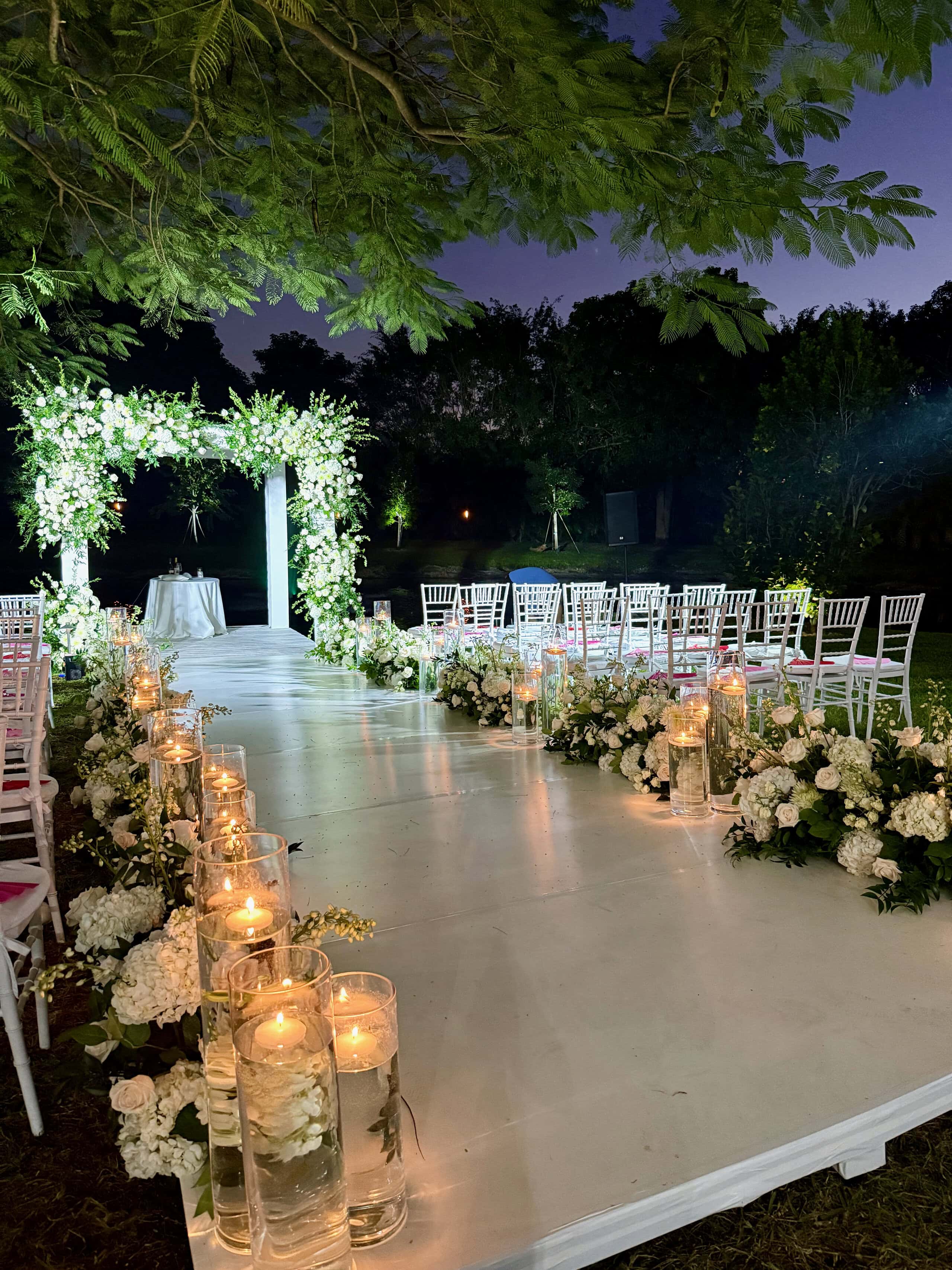 Waterside outdoor wedding ceremony with floral aisle and candle décor at Saint Patrick Palace in South Florida.