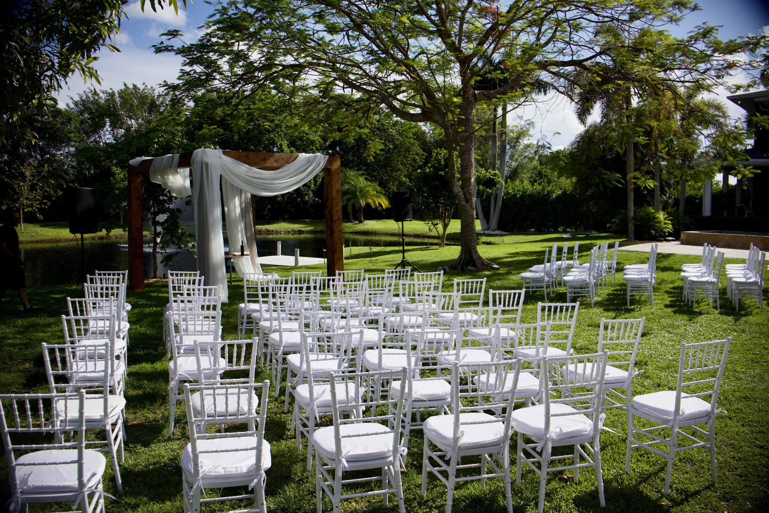 Outdoor waterfront wedding ceremony with white Chiavari chairs at Saint Patrick Palace in Davie, Florida.