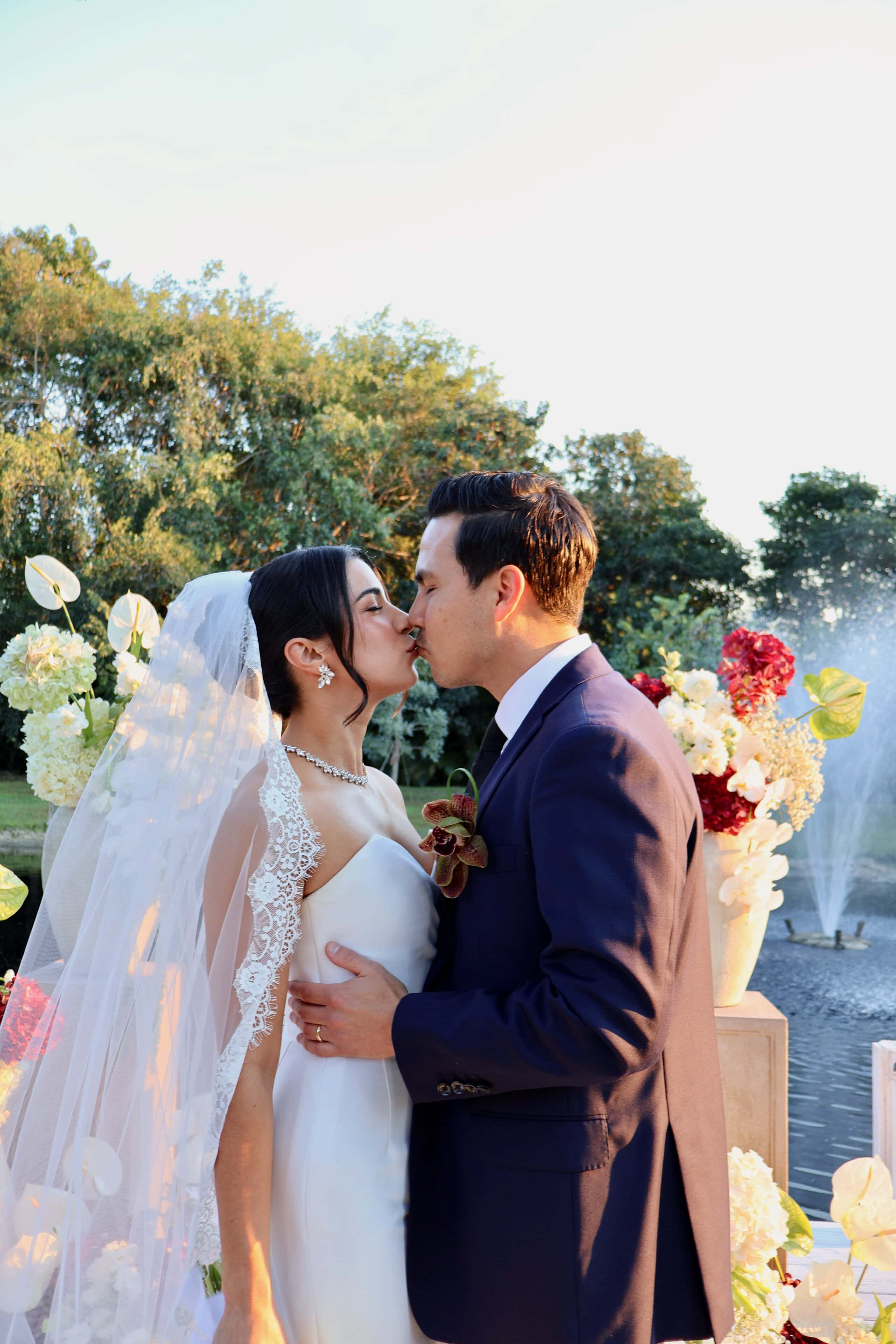 Bride and groom sharing their first kiss during a lakeside wedding ceremony at Saint Patrick Palace.
