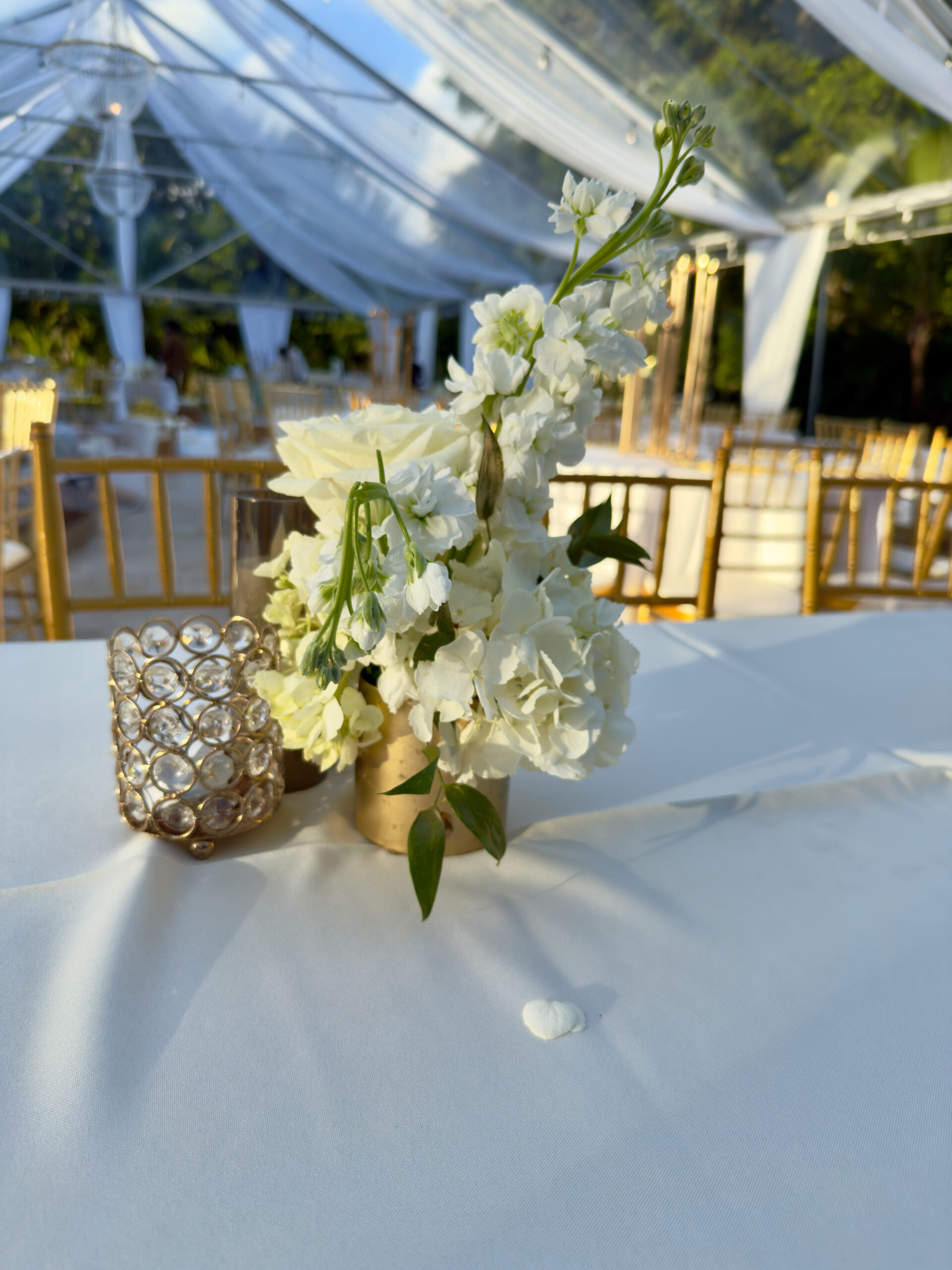 White floral centerpiece and gold candle holder on ivory linen table at 60th birthday celebration in Miami.